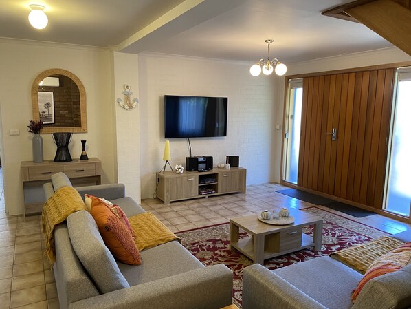A modern living room with a grey sofa set, a wooden cabinet with a flat-screen TV, and a large sliding door.