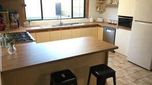 A modern kitchen with a wooden countertop, a sink, a stove, and a refrigerator. There are two stools and a window with a view of the outside. - Dromana Charmer - Large family home, 8 min easy walk to the beach. (Dromana)