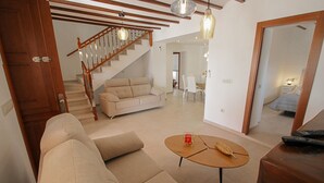 A living room with a sofa, coffee table, and a staircase leading to another room. - Rosalia - holiday home with panoramic view and private pool in Teluda (Teulada)