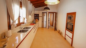 A modern kitchen with a stainless steel refrigerator, a built-in oven, and a large pendant light. - Rosalia - holiday home with panoramic view and private pool in Teluda (Teulada)