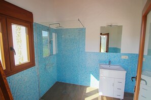 Uma casa de banho com azulejos de mosaico azul, chuveiro, lavatório e espelho.