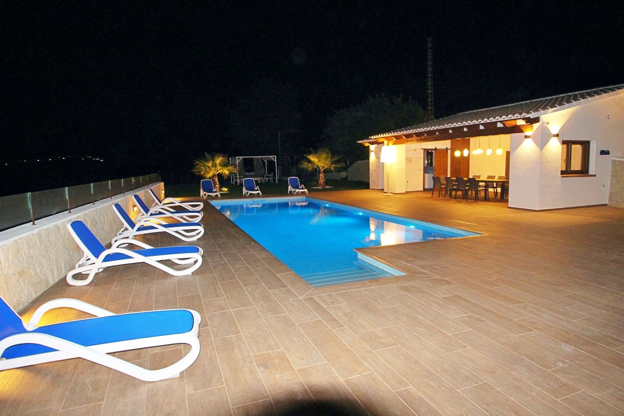 Ein Schwimmbecken mit Liegestühlen und einer überdachten Sitzgelegenheit bei Nacht.