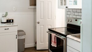 A compact kitchen with white cabinetry, a stainless steel oven, and a ceiling fan.