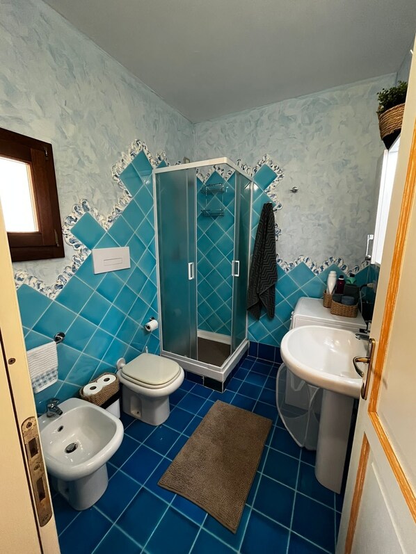 A bathroom with a shower, toilet, bidet, sink, and blue tiled walls. - A little piece of paradise... (Pittulongu)