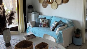 Una sala de estar con un sofá azul, decoración en la pared, una mesa blanca con cestas y vistas al exterior.