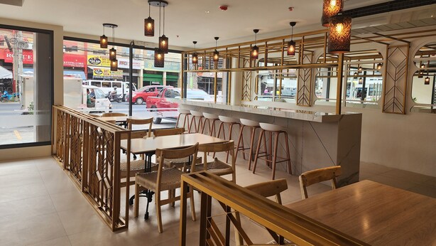 A modern restaurant with wooden furniture, hanging pendant lights, and a view of the street outside. - TRAVELITE EXPRESS HOTEL LA UNION (San Fernando)