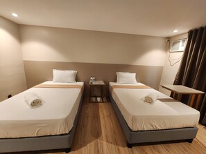 A hotel room with two single beds, a small bedside table with toiletries, a wooden floor, and a window with curtains. - TRAVELITE EXPRESS HOTEL LA UNION (San Fernando)