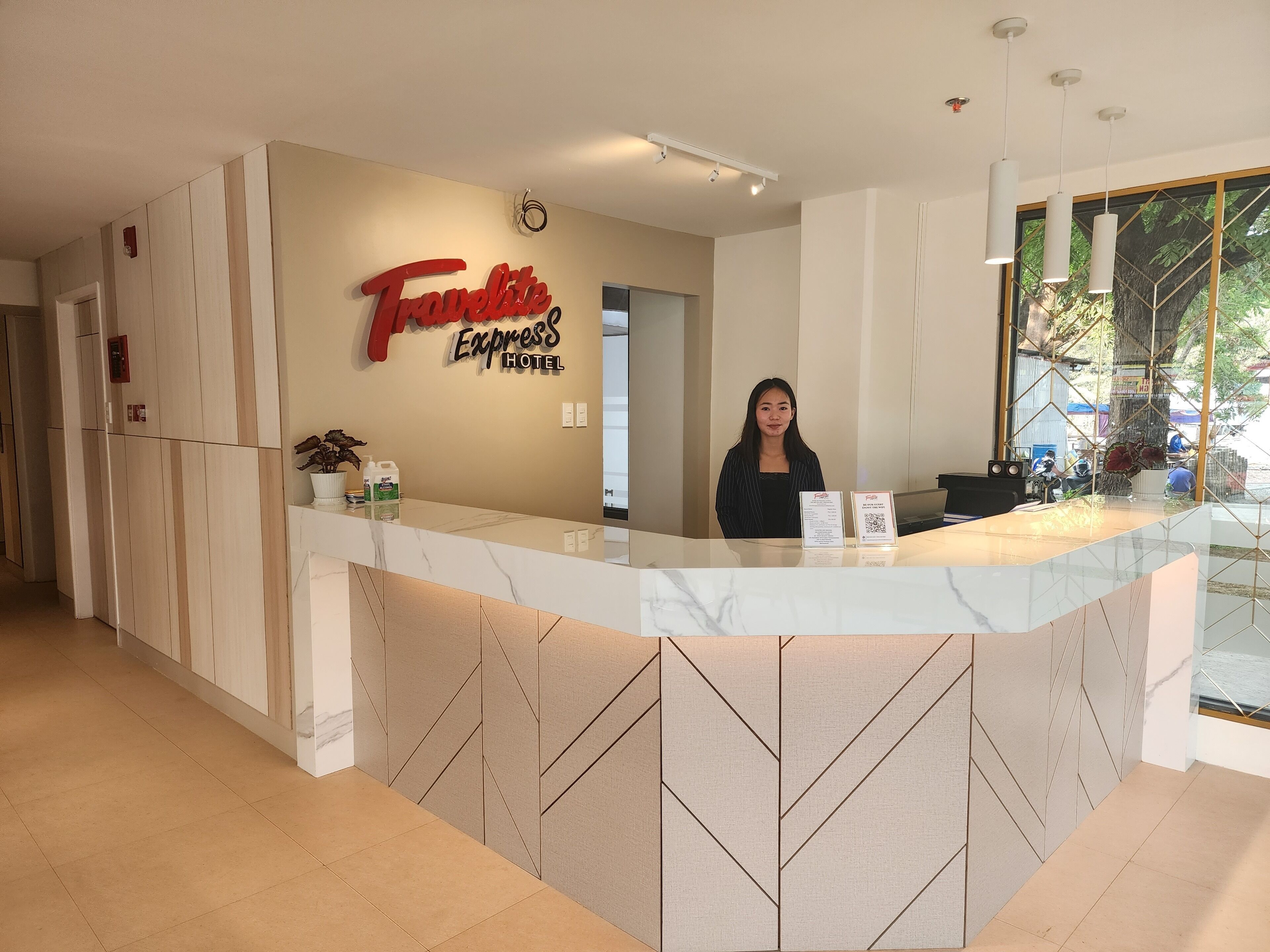 A reception desk at Travellite Express Hotel with a modern design, a large window offering a view of the outdoors, and a sign indicating the hotel's name.