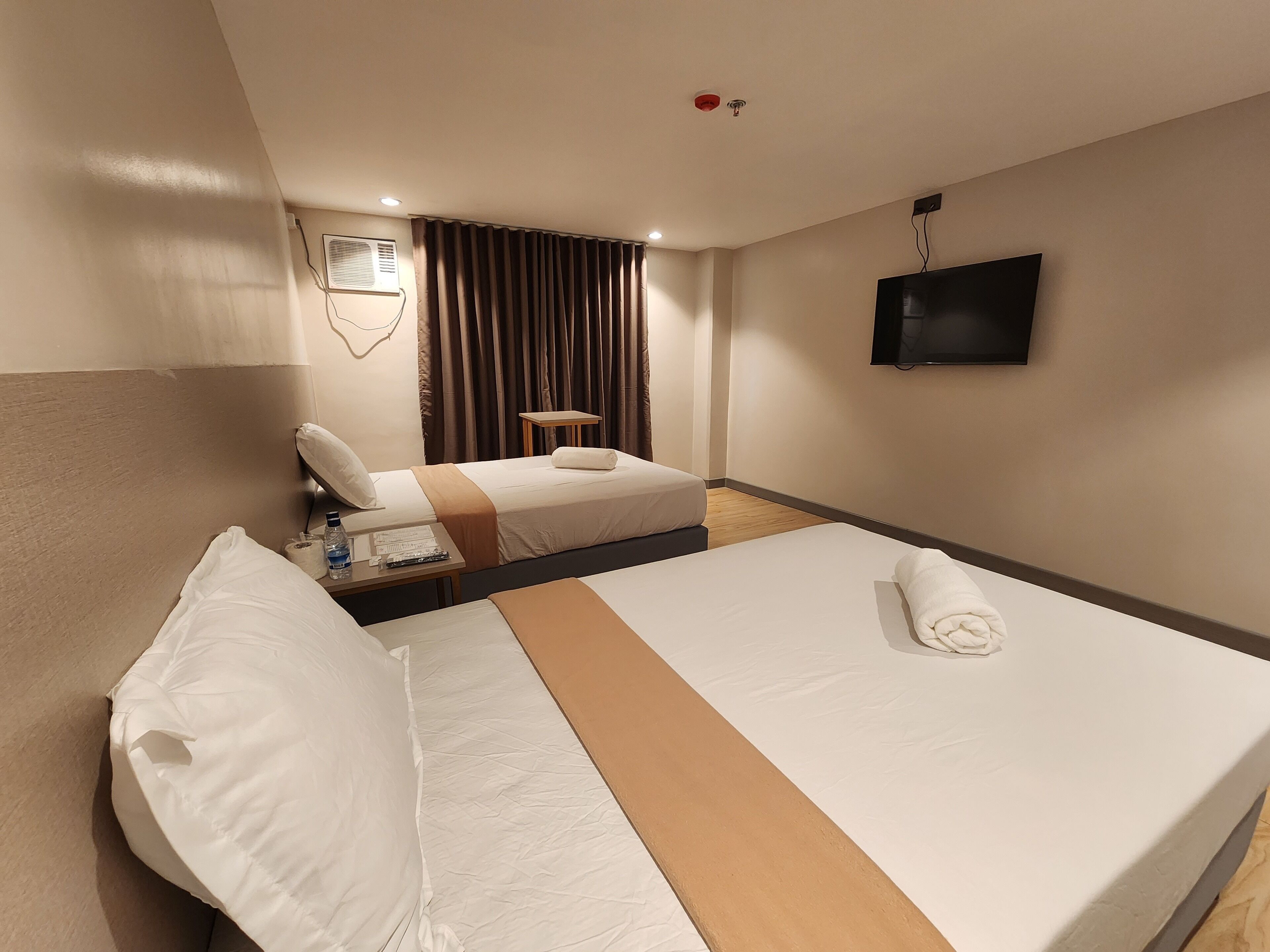 Une chambre d’hôtel avec un grand lit, un plus petit lit, une télévision et une fenêtre avec des rideaux.