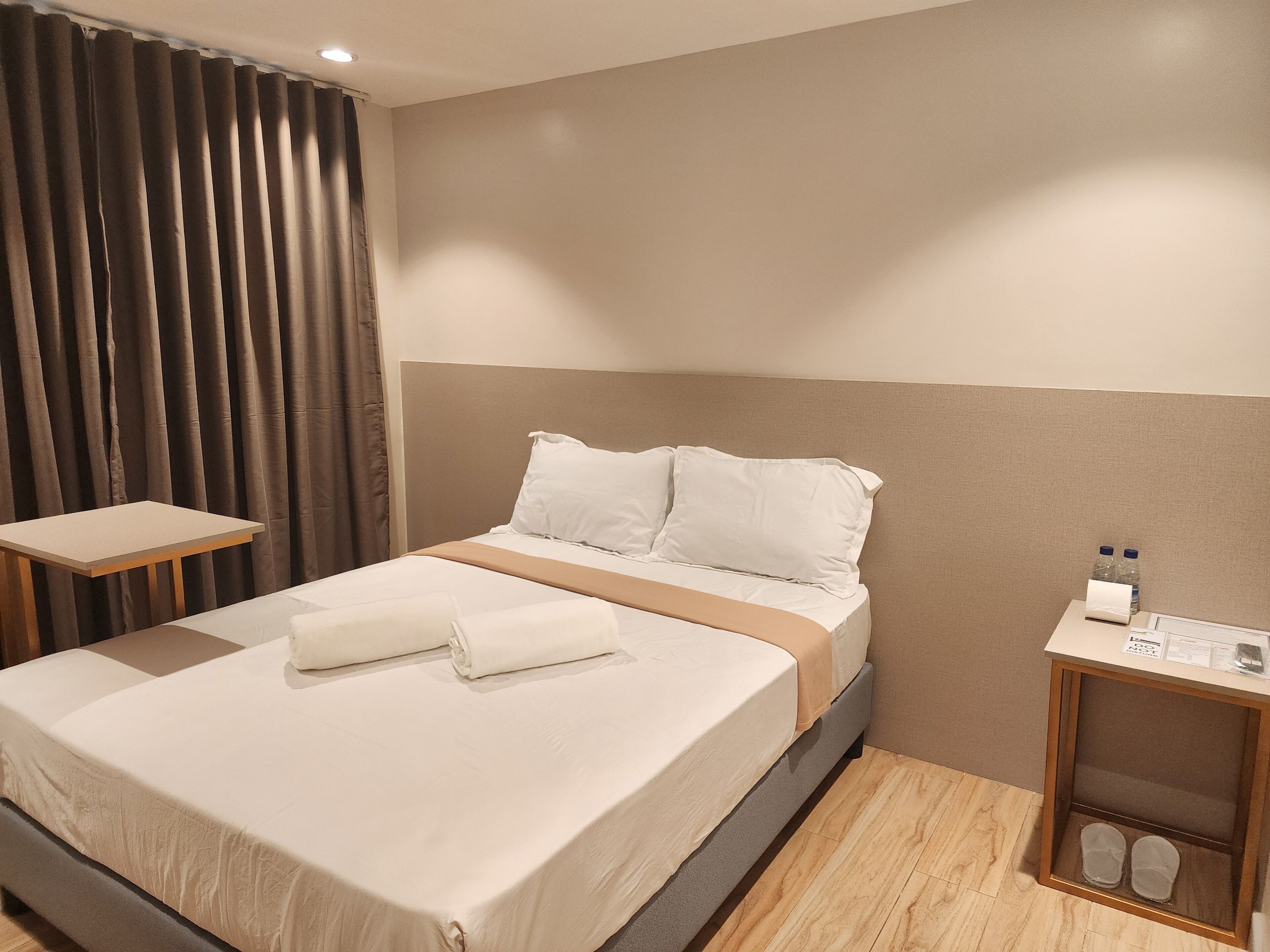 A neatly made bed with white linens, a wooden nightstand with toiletries, and a shoe rack.