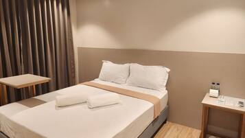 A neatly made bed with white linens, a wooden nightstand with toiletries, and a shoe rack.