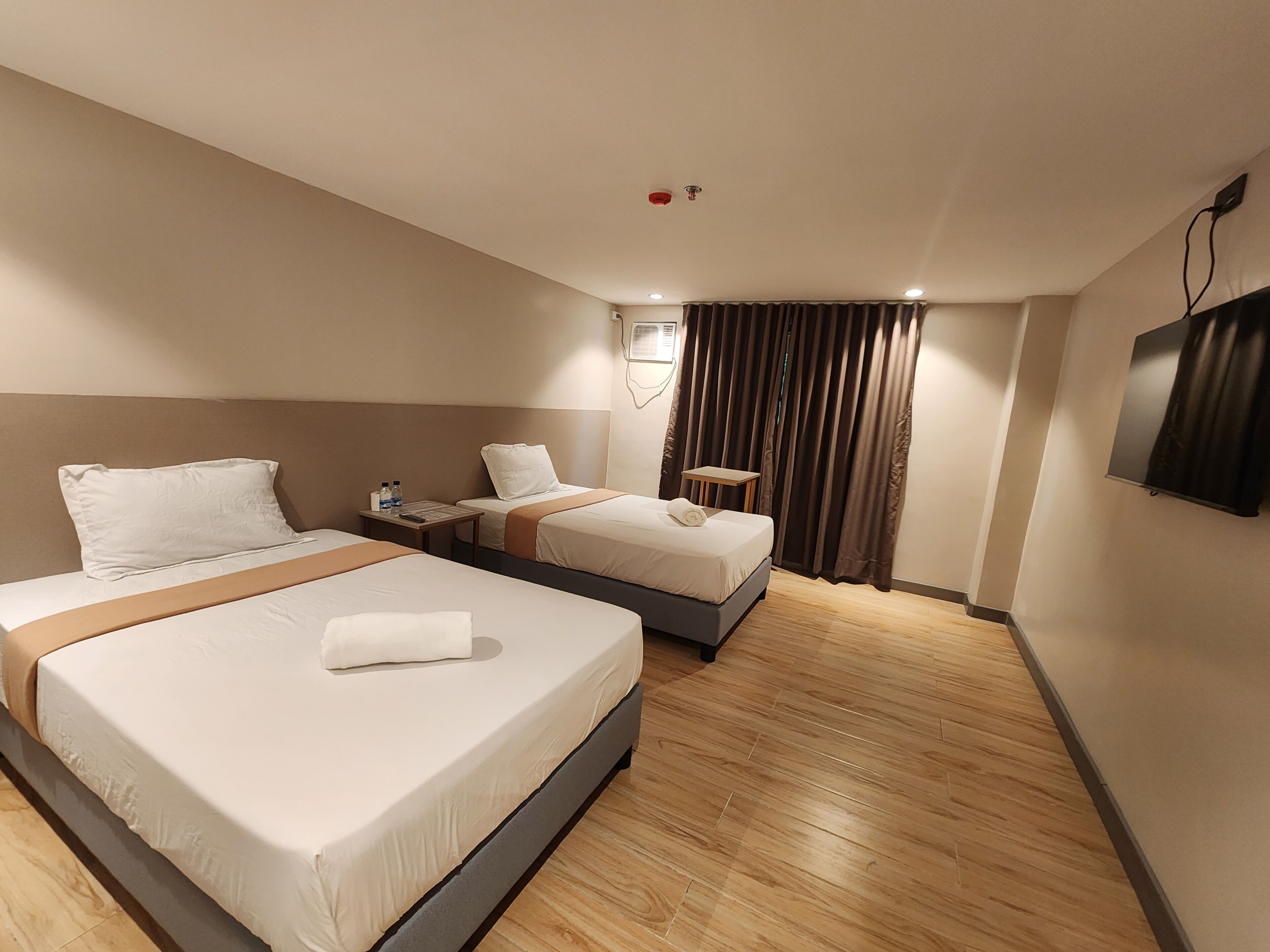 Habitación de hotel con dos camas, una mesita, televisión y ventana con cortinas.