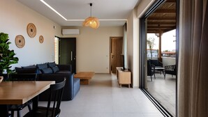 Una sala moderna con sofá, mesa de comedor, sillas, una mesa baja de madera y una lámpara colgante.