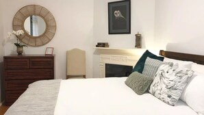 Quarto com uma cama grande, cômoda, espelho, quadro de uma coruja emoldurada, lareira e uma cadeira.