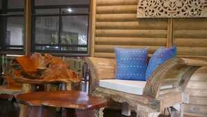 A rustic wooden interior with a carved wooden bench and table, a cushioned bench with patterned cushions, and a decorative wall panel. - Romantic rainforest retreat with magical waterfall (Cow Bay)