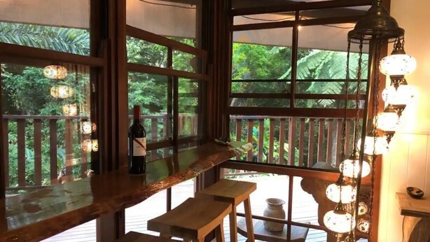 A wooden deck with a bar area, large windows, and hanging light fixtures. - Romantic rainforest retreat with magical waterfall (Cow Bay)