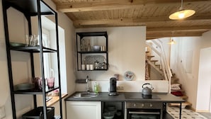 A compact kitchen with a built-in oven, a sink, and a black countertop. There are shelves with dishes and a kettle on the counter. - Kutscherhaus / Stadthaus Usedom (Usedom)