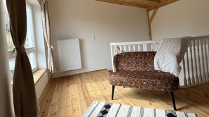 A room with a wooden ceiling, a radiator, a patterned sofa, and a window with curtains. - Kutscherhaus / Stadthaus Usedom (Usedom)