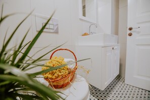 A bathroom with a white sink, a white toilet, and a basket of yellow flowers on the floor. - Tin Ada (Bozcaada)