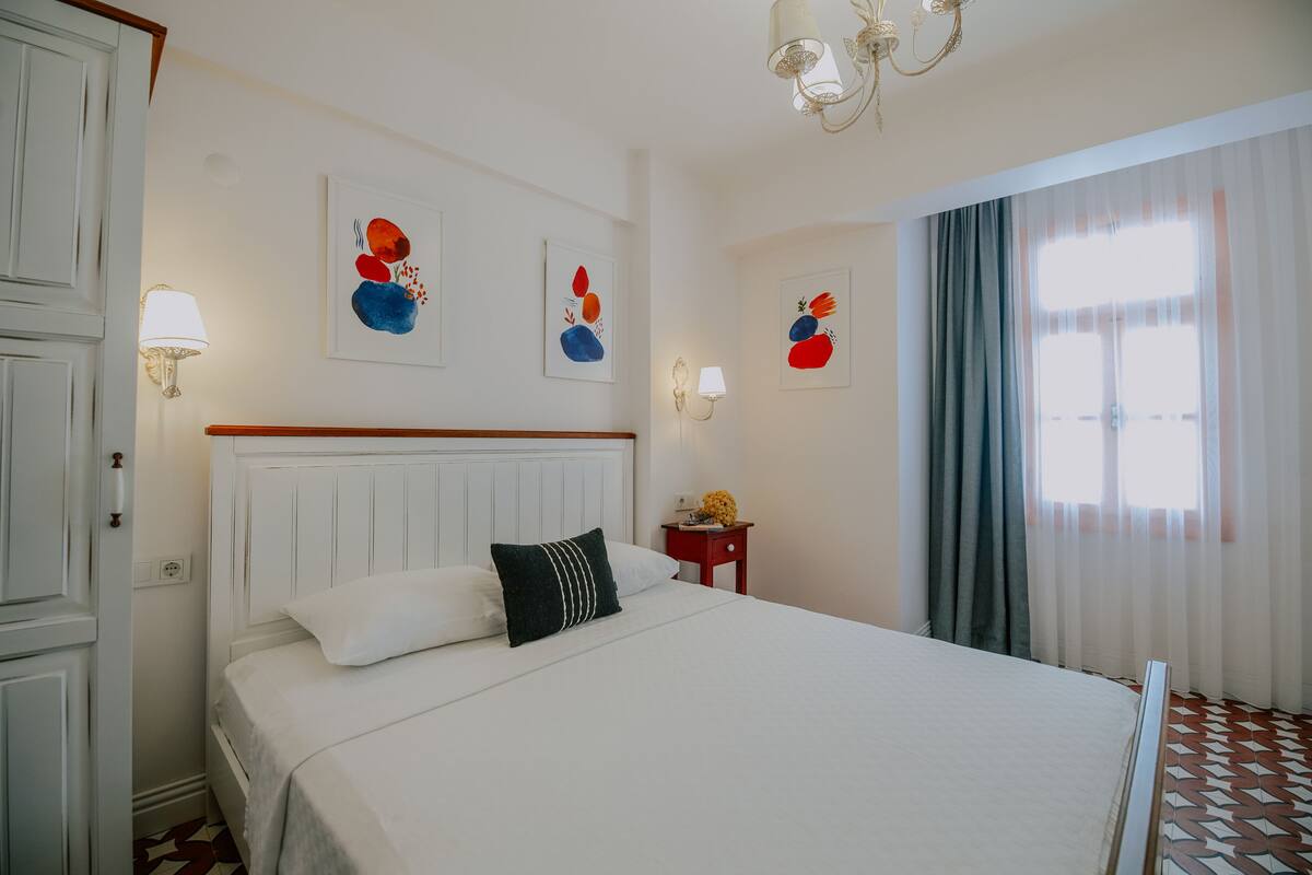 A hotel room with a large bed, white walls, and artwork on the walls.