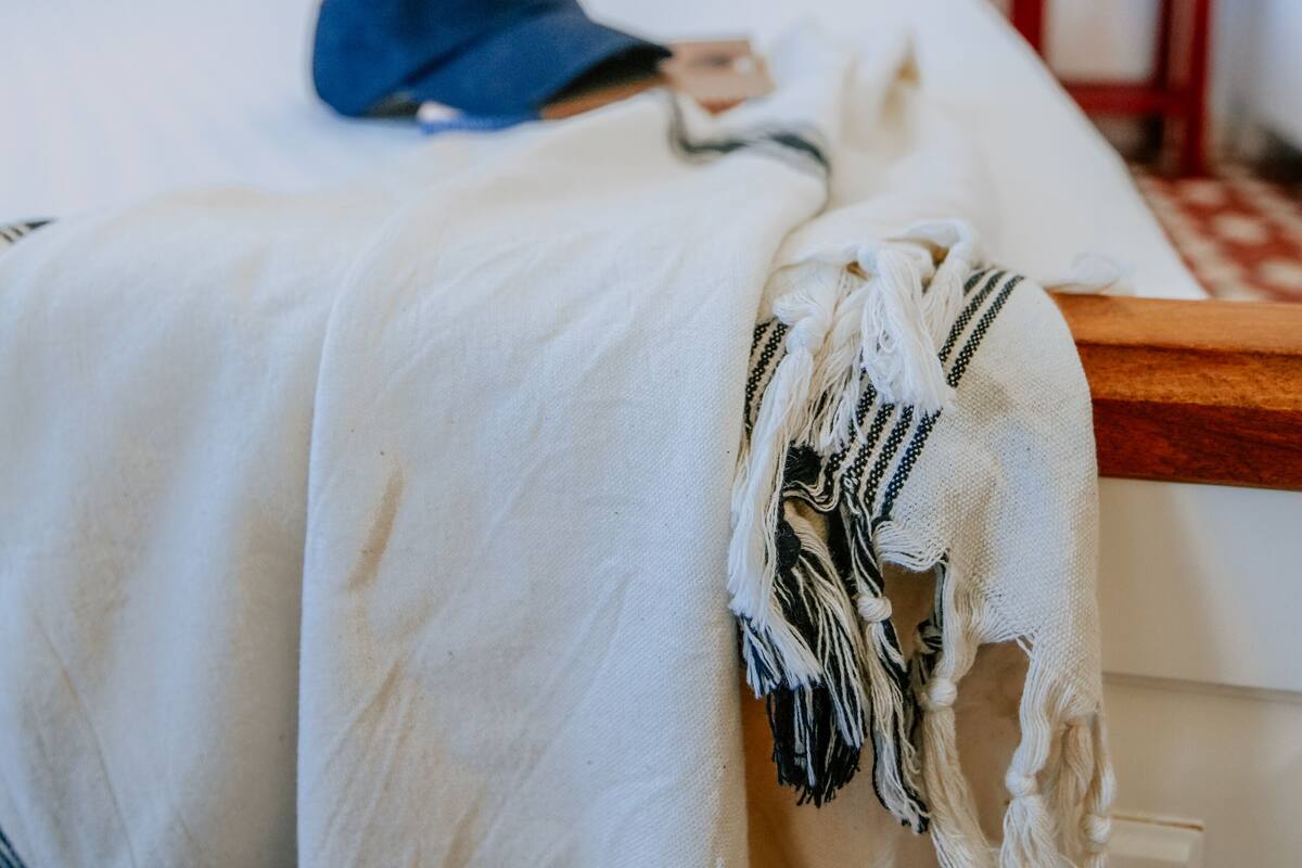 A neatly made bed with a white blanket and a blue cap on it. There are three wall art pieces above the bed.