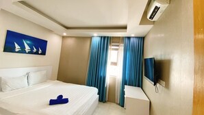 Une chambre d’hôtel avec un lit, un tableau représentant des voiliers, une télévision et un appareil de climatisation.