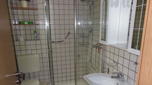 Ein Badezimmer mit einer Duschkabine, einem weißen Waschbecken, einer Toilette und einem Spiegel über dem Waschbecken.