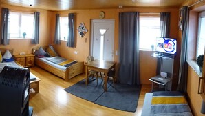 Ein gemütlicher Raum mit Bett, Schreibtisch, Stuhl, Fernseher und einem fenster mit Vorhängen.