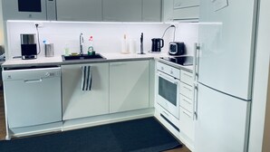 A modern kitchen with white cabinetry, a built-in microwave, a coffee maker, a toaster, and a refrigerator. - Completely new designer apartment on the ground floor with a spacious patio (Espoo)