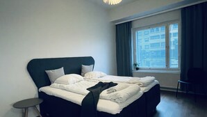 A neatly made bed with white bedding and a dark headboard in a room with wooden flooring. - Completely new designer apartment on the ground floor with a spacious patio (Espoo)