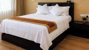 A neatly made bed with white bedding and a brown accent, a bedside table with a lamp, and a power outlet on the wall.