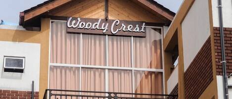 A building with a sign reading 'Woody Crest' and a balcony with a railing.