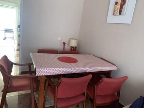 A dining area with a square table covered by a patterned tablecloth, surrounded by six red chairs. - Dog welcome at this cosy home near to beach shops bars and restaurants and park. (Torrevieja)