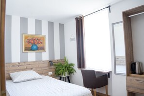 A bedroom with a bed, a desk, a chair, a potted plant, a painting, and a window with curtains. - Hiša Poljana (Prevalje)