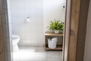 A bathroom with a toilet, a roll of toilet paper, a potted plant, and a shelf with towels. - Hiša Poljana (Prevalje)