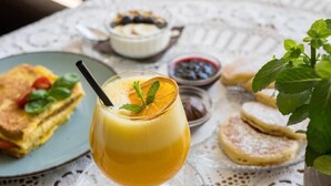 A breakfast setting with a glass of orange juice, a plate of pancakes, and a bowl of blueberries. - Hiša Poljana (Prevalje)