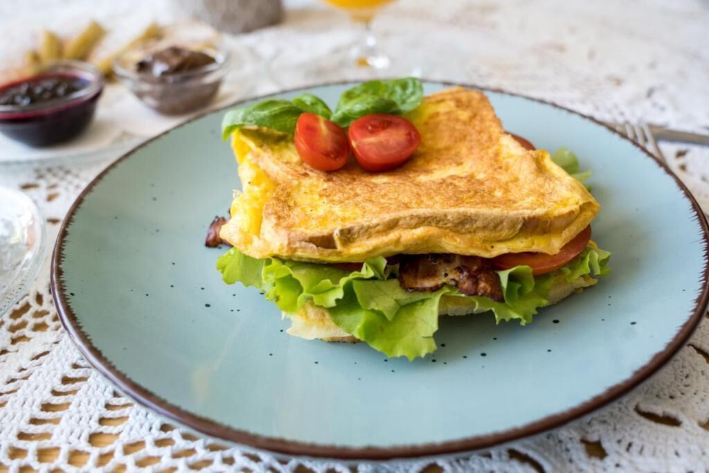 A sandwich on a plate with lettuce, tomatoes, and a fried egg.