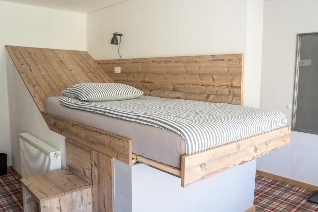 A loft-style bedroom with a slanted ceiling, a wooden headboard, a bed with striped bedding, and a small wooden bench.
