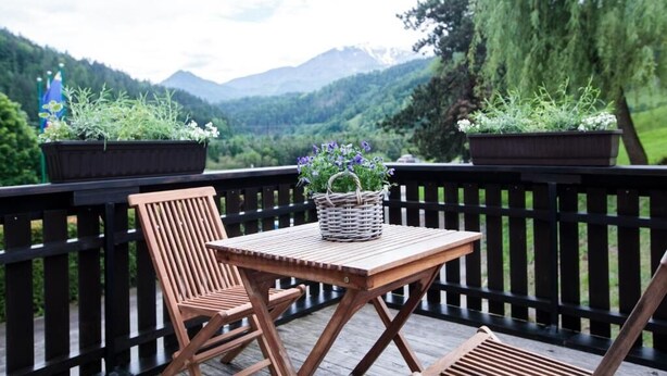 A wooden deck with a table and chairs, surrounded by potted plants and a view of mountains. - Hiša Poljana (Prevalje)