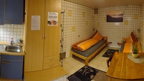 Ett litet rum med en säng, ett litet bord, ett handfat och ett skåp.