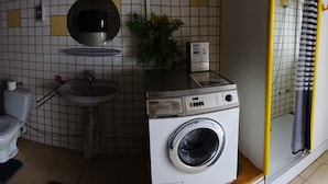 Ett litet badrum med toalett, handfat, tvättmaskin och en duschhörna.