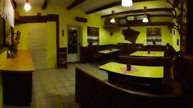 Interior de restaurante con mesas y bancos de madera, suelo de baldosas y lámparas colgantes.