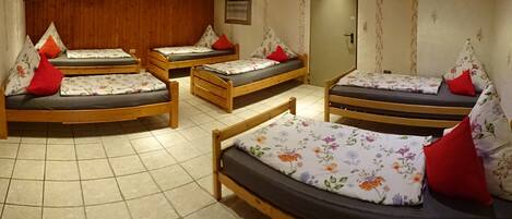 A room with four wooden beds, each with floral bedding and red pillows.