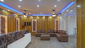 A modern reception area with a marble counter, a brown leather sofa, and a ceiling fan. - Hotel Fortune Stay (Ghaziabad)