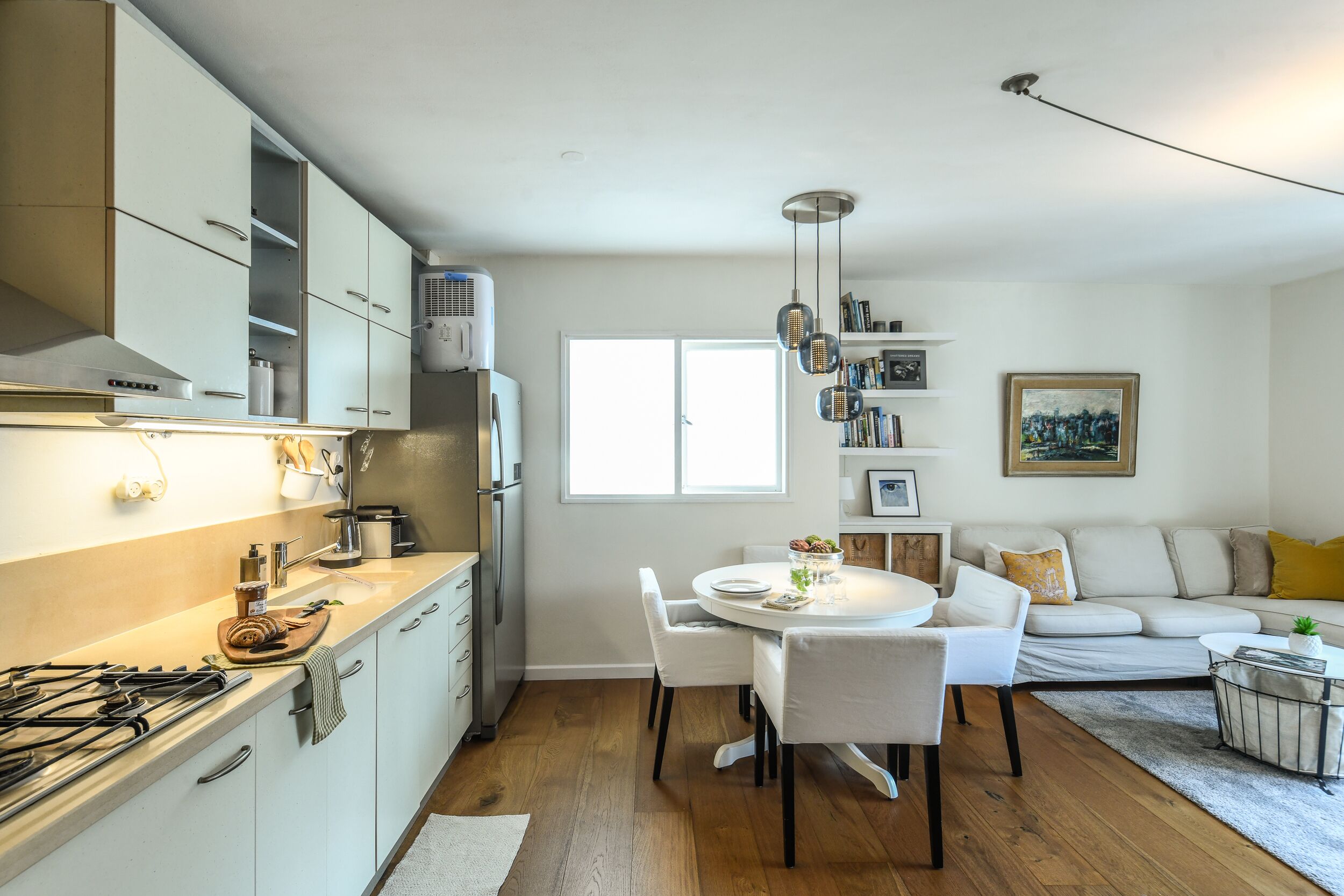 A modern kitchen with white cabinets, a dining area with a round table and chairs, and a living room with a sofa and a coffee table.