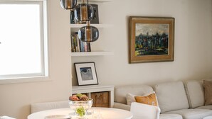 Un salon moderne avec une table ronde blanche, un canapé et une bibliothèque contenant des livres et des objets décoratifs.