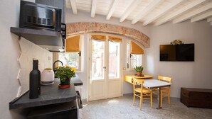 A compact kitchen with a built-in microwave, a coffee maker, and a potted plant. There is a dining area with a table and chairs, and a small wooden cabinet. - Casa Priscilla (Salò)