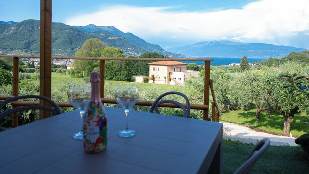 A table with a bottle and two glasses, overlooking a mountainous landscape with a building in the distance. - Casa Priscilla (Salò)