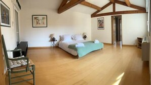 Een ruime slaapkamer met een groot bed, houten vloeren en zichtbare houten balken.