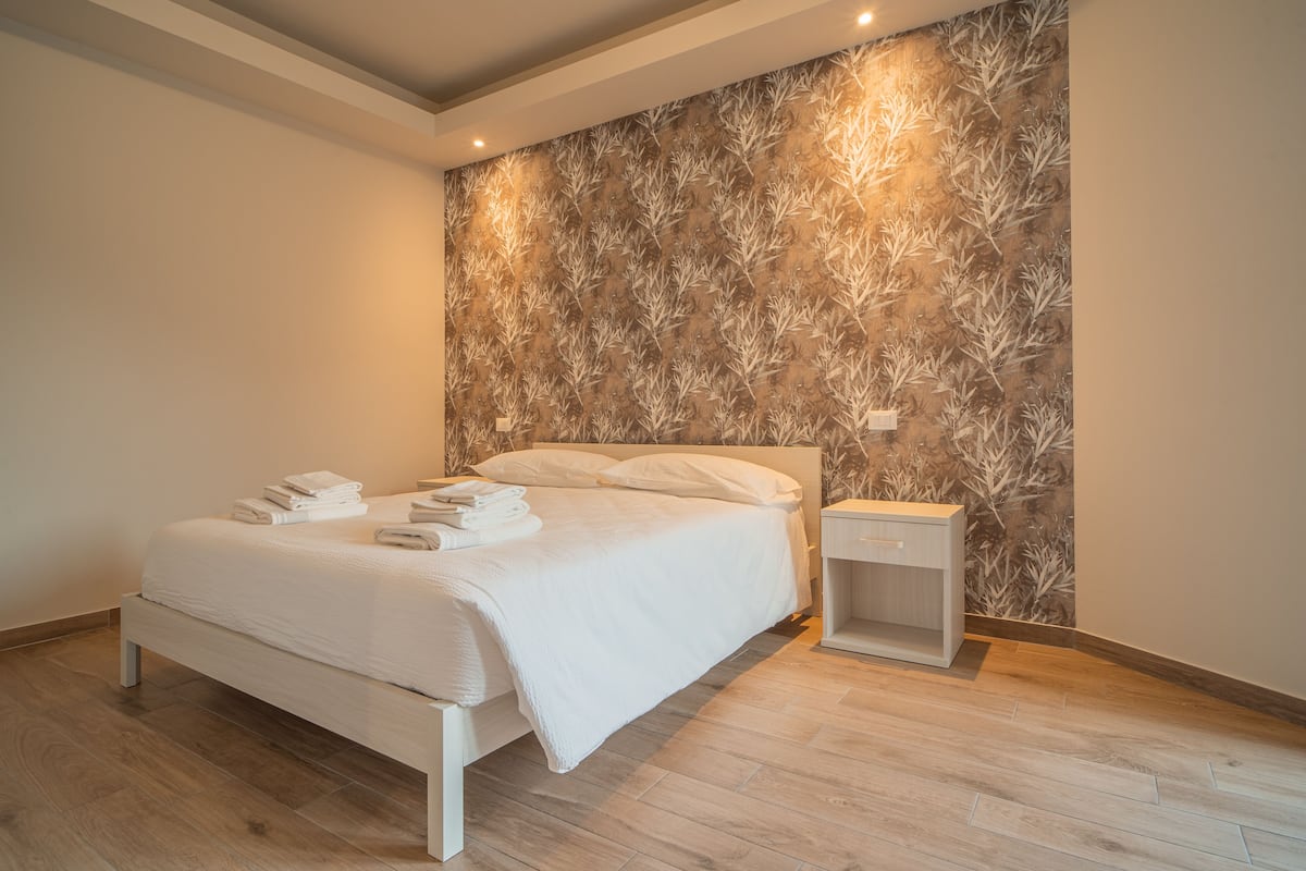 A modern bedroom with a bed, a nightstand, and a wall with a leaf pattern.